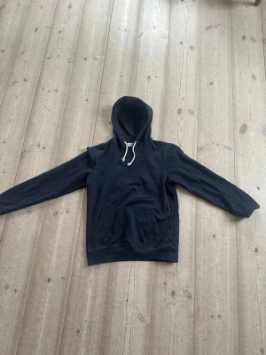 Marinblå hoodie med ficka och dragsko - En stilren marinblå hoodie med vita dragsnören. Hoodien har en stor magficka framtill och ribbade muddar vid ärmslut och nederkant. Perfekt för en avslappnad look och enkel att matcha med jeans. Hoodien är från pier one och är i storlek S