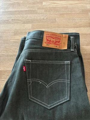 Levi's 501 mörkgröna jeans - Klassiska Levi's 501 jeans i en snygg mörk färg med raka ben och vit kontrastsöm. Jeansen har fem fickor, knappgylf och den ikoniska röda Levi's-lappen på bakfickan. Tillverkade i slitstark bomull, perfekta för en avslappnad och tidlös stil. Köpta i usa använda en gång skriv mer för frågor !!