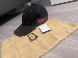 Svart  canvas keps - Snygg svart keps från  med klassiskt monogram över hela kepsen. På sidan finns en ikonisk grön och röd rand. Kepsen har böjd skärm och justerbar passform. 