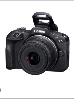 Canon EOS R100systemkamera svart - Canon EOS systemkamera i svart med robust grepp, stor LCD-skärm och inbyggd blixt. Kameran har ett modernt och stilrent utseende med tydliga knappar och en lins i plast och metall. Perfekt för dig som vill ta snygga bilder och utforska fotografering.