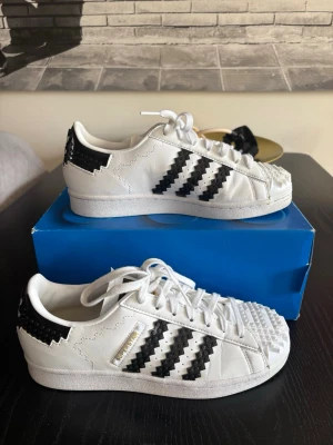 Adidas x LEGO Superstar sneakers - Unika Adidas x LEGO Superstar sneakers i vitt och svart med klassiska tre ränder och LEGO-detaljer på häl och tå. Lågt skaft, snörning och cool design som sticker ut. Använda ett par gånger och är i väldigt bra skick!