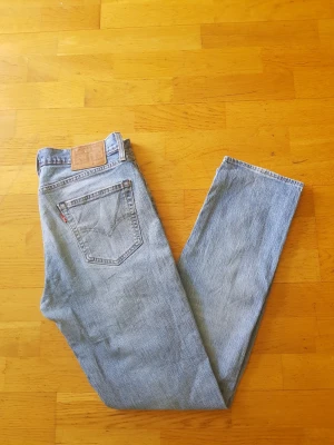 Levi's 511 - Klassiska ljusblå jeans från Levi's 511  med rak passform och femficksdesign. Jeansen har den ikoniska läderpatchen bak i midjan och röd Levi's-tagg på bakfickan. Tillverkade i slitstark denim, perfekta för en avslappnad och tidlös stil.
