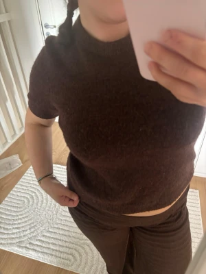 Brun stickad kortärmad topp - Mysig brun stickad topp med korta ärmar och rund halsringning. Modellen är något croppad och har en enkel, stilren design som passar perfekt till många olika outfits.