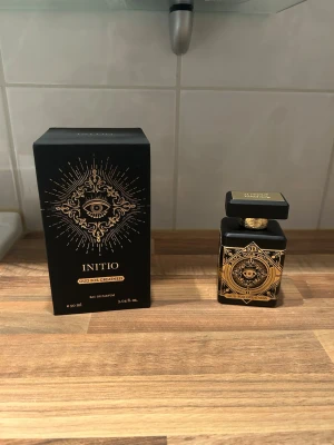 Initio Oud For Greatness parfym 90ml - Lyxig parfym från Initio, Oud For Greatness, i en svart fyrkantig flaska med detaljer i guld och mystiskt ögonmotiv. Flaskan rymmer 90 ml och har en elegant, matt finish med exklusiv känsla. Kommer i matchande svart och guld ask.