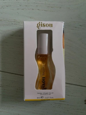 Gisou Honey Infused Lip Oil duo - Säljer två läppoljor från Gisou, båda i vågformade genomskinliga förpackningar. Ena är i färgen honey gold och den andra i milky mocha. Båda innehåller 8 ml och har en lyxig känsla med guldiga detaljer. Perfekt för dig som vill ha återfuktade och glansiga läppar.