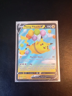 Pokémonkort Flying Pikachu V 25th - Säljer ett Pokémonkort Flying Pikachu V från 25-årsjubileet. Kortet har en färgglad design med Pikachu som flyger med ballonger. Framsidan visar attackerna Thunder Shock och Fly. Kortet är i plastficka och har jubileumslogga på baksidan. Fraktas i plastfodral.
