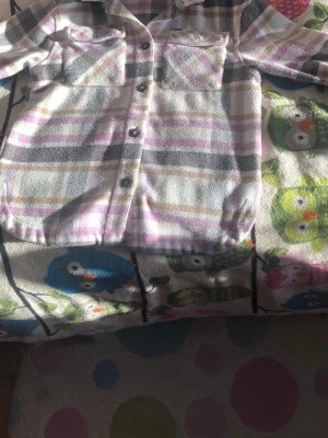 Lila-rutig overshirt med fickor - Overshirt i mjukt tyg med lila, grå och vita rutor. Två stora bröstfickor med lock och knappar framtill. Rak passform och klassisk krage. Perfekt lager-på-lager-plagg för en avslappnad stil.