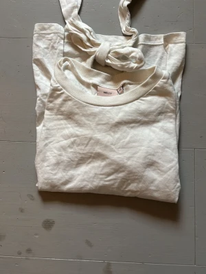 Vit omlottopp med knyt i ryggen - Snygg vit topp från Nelly med omlottdesign och knyt i ryggen. Toppen har korta, vida ärmar och är gjord i mjuk bomull.