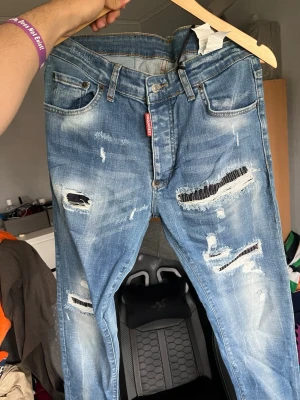 Dsquared2 d2 Blå slitna jeans från  - Priser kan diskuteras. Säljer ett par blå jeans från Dsquared2 med coola slitningar och trasiga detaljer. Jeansen har klassisk femficksmodell, knappgylf och tydliga slitningar framtill för en trendig look. Perfekta för dig som gillar streetstyle och vill sticka ut.