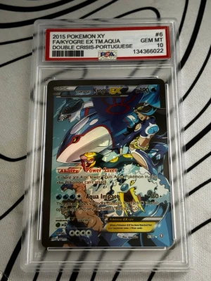 Pokémonkort Kyogre EX PSA 10 - Säljer ett samlarkort från 2015 Pokémon XY, Kyogre EX Team Aqua Double Crisis på portugisiska. Kortet är graderat PSA 10 GEM MT och ligger i ett genomskinligt plastskydd. Färgstark design med blå, vit och röd illustration. OBS KORTET ÄR FEJK!!!