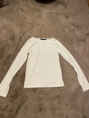 Vit ribbad långärmad topp - Har aldrig använts. Säljer en stilren vit långärmad topp i ribbat material. Toppen har rund halsringning och är figurnära med långa ärmar. Perfekt att matcha med jeans eller kjol för en enkel och snygg look