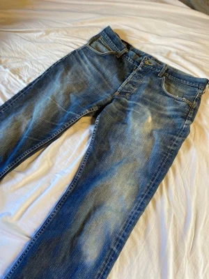 Blå Lee jeans med slitningar - Snygga blå jeans från Lee med klassisk femficksmodell och coola slitningar på benen. Jeansen har raka ben och tydliga kontrastsömmar. Perfekta för en avslappnad och trendig look.