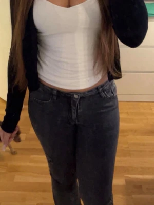 Mörk grå Bootcut jeans med mid/low waist - Säljer ett par svarta jeans medbootcutpassform och low/mid midja. Jeansen har klassisk femficksdesign och stängs med knapp och dragkedja. Perfekta till en avslappnad stil och passar till det mesta i garderoben.