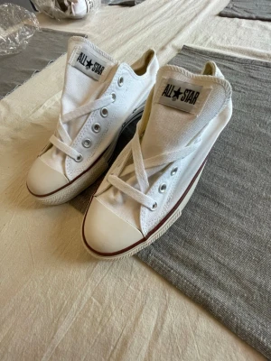 Vita Converse All Star låga sneakers - Klassiska vita Converse All Star sneakers i canvas med lågt skaft och vit gummisula. Skorna har den ikoniska All Star-loggan på plösen och silverfärgade öljetter. Perfekta för en avslappnad och stilren look.