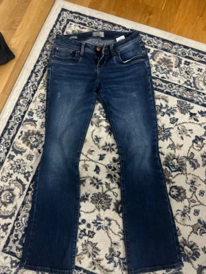 Mörkblå bootcut jeans från LTB - Snygga mörkblå bootcut jeans från LTB med klassisk femficksdesign och subtila slitningar framtill. Jeansen har en låg midja och är tillverkade i stretchigt denim för extra komfort. Perfekta för en avslappnad och trendig look.