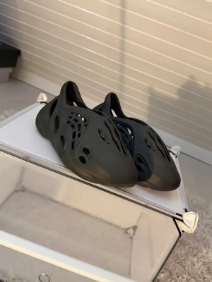 Svarta Yeezy Foam Runner tofflor - Säljer ett par svarta Yeezy Foam Runner i storlek 42. Skorna är helt oanvända och i nyskick, säljs endast på grund av att de inte passar.  Väldigt populära och bekväma slip-on sneakers med unik design som funkar både till vardags och som statement-piece.  Storlek: 42 Färg: Svart Skick: Oanvända Originalbox: Saknas Pris: 799 kr