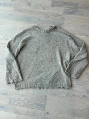 Beige stickad tröja med rund hals - En enkel och stilren beige stickad tröja med rund hals och långa ärmar. Tröjan har en rak passform och ribbstickade detaljer vid hals, ärmslut och nederkant. Perfekt för lager-på-lager och en avslappnad look.