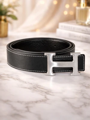 H-bälte - Stilrent svart skärp från i skinn med ett stort, silverfärgat H-spänne. Skärpet har vita kontrastsömmar längs kanterna som ger en snygg detalj. Perfekt accessoar för att lyfta din outfit.