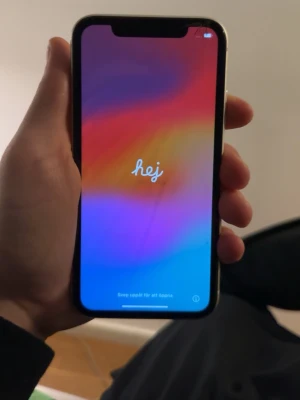 Vit iPhone 11 med dubbla kameror - Snygg vit iPhone 11 med stilren design och rundade kanter. Telefonen har dubbla kameror på baksidan och Apples klassiska logga i mitten. Skärmen är stor och täcker nästan hela framsidan och en liten spricka vid hörnet men inget som påverkar och perfekt för sociala medier och streaming och ligger på 76% batterihälsa men håller länge ändå