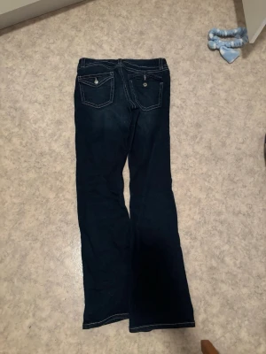 Mörkblå bootcut jeans Gina Tricot - Mörkblå jeans från Gina Tricot med bootcut-modell och kontrastsömmar. Jeansen har två bakfickor med lock och knappdetaljer. Perfekta för dig som gillar en klassisk och avslappnad stil. Pris kan diskuteras 