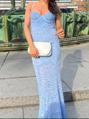 Ljusblå glittrig långklänning - Supersnygg ljusblå långklänning med tunna axelband (som går att ta av), och glittriga paljetter över hela klänningen. Figurnära passform med markerad byst och lätt utsvängd nederdel. Perfekt för bal eller festkvällar.