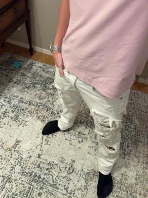 Vita ripped jeans storlek W31 L32 - Säljer ett par vita jeans med flera slitningar och hål på benen för en trendig, avslappnad look. Jeansen har fransiga benslut och klassisk femficksmodell med nitar. Perfekta för dig som gillar streetstyle och vill sticka ut.