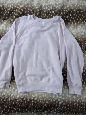 Ljuslila hoodie utan huva - En basic ljuslila sweatshirt med rund halsringning och långa ärmar. Tröjan har en enkel och avslappnad passform, ribbade muddar vid ärmslut och nederkant. Perfekt för en chill och stilren look.