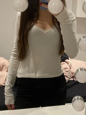 Vit ribbad långärmad topp - Säljer en vit långärmad topp med v-ringning och spetsdetalj vid halsen. Toppen har en fin passform och är perfekt att styla med både jeans och kjol. Superenkel men ändå snygg och passar till många olika looks.💗