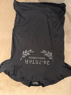 Svart t-shirt från Dsquared2 - Säljer en svart t-shirt från Dsquared2 med tryck i grått framtill och dekorativa lagerblad. Klassisk passform och rund halsringning. Tillverkad i Italien och gjord av mjuk bomull, perfekt för en avslappnad och stilren look.