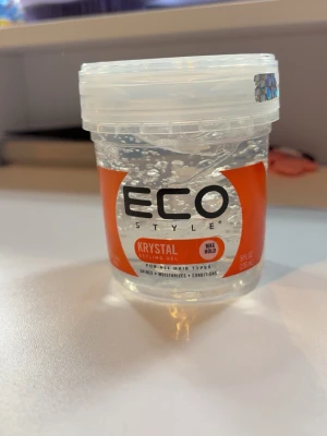 Eco Style Krystal Styling Gel - Helt oanvänd. Eco Style Krystal Styling Gel är en genomskinlig hårgel i plastburk med röd etikett. Gelen ger max stadga och passar alla hårtyper. Perfekt för att forma och hålla frisyren på plats samtidigt som den återfuktar och ger glans.