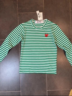 Randig långärmad topp Comme des Garçons - Grön och vit randig långärmad topp från Comme des Garçons PLAY med rund halsringning och det ikoniska röda hjärte-emblemet på bröstet. Storlek S. Lånad bild💞
