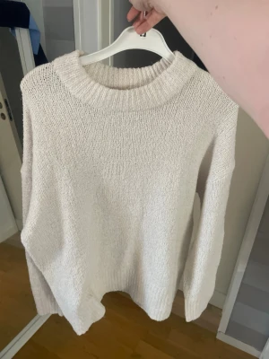 Beige oversized stickad tröja - Säljer en beige oversized stickad tröja med grovstickad struktur och bred ribbad halsringning. Tröjan har långa ärmar och avslappnad passform, perfekt för lager på lager och en chill look.