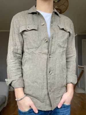 Lindbergh linen overshirt – S - Beige/khaki overshirt i linne från Lindbergh. Sjukt clean piece som passar till allt – perfekt till våren och sommaren.  • Storlek: S • Material: Linne • Skick: Väldigt bra • Färg: Beige/khaki • Passform: Regular • Funkar både öppen och knäppt  🔥 Trendig och lätt att styla – säljes pga rensning  