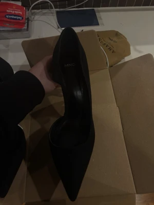Svarta pumps från Mango med spetsig tå - Stilrena svarta pumps från Mango med spetsig tå och öppen sida, 9cm klack. Klackarna har en elegant siluett och är tillverkade i ett matt material som ger en lyxig känsla. Perfekta för att lyfta vilken outfit som helst.