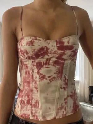 Rödvit tie-dye korsett med smala axelband - Trendig korsett från PrettyLittleThing i röd och vit tie-dye. Modellen har smala justerbara axelband, markerade kupor och synliga sömmar för en snygg siluett. Perfekt för att lyfta vilken outfit som helst. Materialet är mjukt och följsamt.
