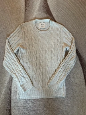 Beige kabelstickad tröja Hollister - Kabelstickad tröja i beige från Hollister med rund halsringning och ribbade muddar vid ärmslut och nederkant. Klassisk och stilren design som passar perfekt till jeans och liknande