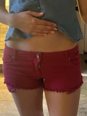 Mörkröda jeansshorts med fransig kant - Snygga mörkröda jeansshorts med fransig kant nertill och klassisk femficksdesign. Shortsen har knapp- och dragkedjestängning samt bälteshällor. Perfekta för sommaren och ger en cool vibe till din outfit.