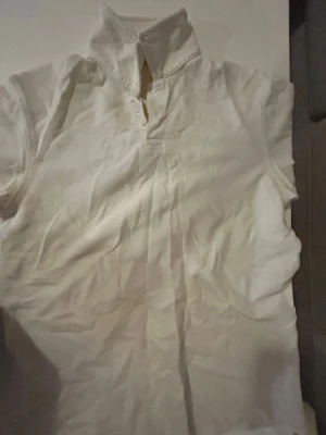 Vit kortärmad Piké - Zara  - Vit t-shirt med korta ärmar och hög krage med knappdetalj framtill. Enkel och stilren design som passar till det mesta. Tillverkad i mjukt bomullsmaterial för skön känsla hela dagen.