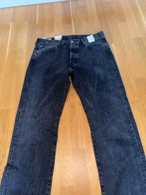 Levi's 501 svarta jeans straight fit - Klassiska svarta Levi's 501 jeans med rak passform och normal midja. Tillverkade i 100% bomull för en autentisk känsla. Femficksmodell med knappgylf och ikonisk läderpatch bak. Perfekta för en avslappnad och tidlös stil.