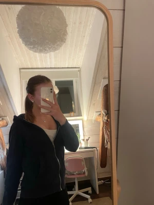 Mörkblå zip-hoodie med huva - Säljer en mörkblå hoodie med dragkedja och huva. Hoodien har ribbade muddar vid ärmslut och nederkant samt fickor på framsidan. Perfekt för att slänga på sig när det är lite kyligt. Materialet känns mjukt och bekvämt.