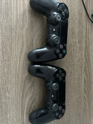 Svarta PlayStation 4 DualShock kontroller - Två svarta DualShock 4 handkontroller från Sony till PlayStation 4. De har klassisk design med touchpad, LED-ljus och ikoniska PlayStation-knappar i färg. Ergonomisk form i plast som ligger skönt i handen, perfekt för gaming och multiplayer. Den ena funkar som vanligt medans den andra kan ha stick-drift. Är osäker på grund av att det var länge sedan jag använde dem.