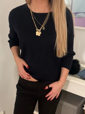 Svart/mörkblå trekvarts tröja med rund hals - En stilren svart/mörkblå tröja med rund halsringning och trekvarts ärmar. Tröjan har en enkel och avslappnad passform, perfekt att matcha med olika outfits. Materialet ser mjukt och bekvämt ut, och modellen har ribbade muddar vid ärmsluten.