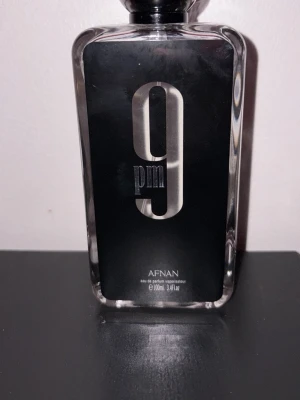Afnan 9PM Eau de Parfum 100ml - Afnan 9PM Eau de Parfum kommer i en stilren, rektangulär glasflaska med svart etikett och stor silverfärgad siffra 9 på framsidan. Flaskan rymmer 100 ml och har en modern, elegant design som sticker ut på parfymhyllan.