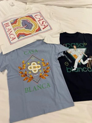 Casa Blanca t-shirts med tryck - Tre t-shirts från Casa Blanca med unika grafiska tryck. En vit med färgglad vågig design, en ljusblå med emblem och löv, samt en svart med tennismotiv. Alla har rund hals och korta ärmar. Perfekta för dig som gillar statement-plagg och coola prints.