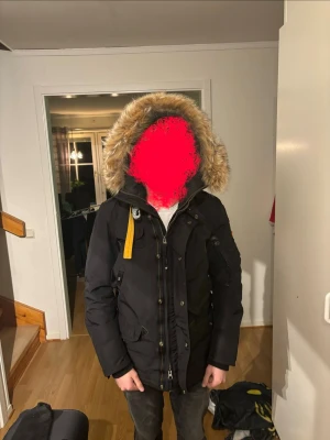 Svart Parajumpers dunjacka med pälskant - Säljer en svart dunjacka från Parajumpers med stor huva och avtagbar pälskant i beige. Jackan har en gul rem vid kragen, flera fickor och robust dragkedja. Perfekt för kalla vinterdagar och riktigt snygg streetstil. Jag säljer denna jackan för att den kommer vara förliten nästa vinter, har bara använt den några gånger 