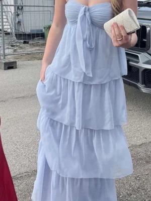 Ljusblå långklänning med volanger - Från Nelly och har utgått från sortimentet Använd 1 gång, endast vid bal.                  Pris kan diskuteras vid smidig affär       Superfin ljusblå långklänning med flera lager volanger och en söt knytning framtill. Klänningen är axelbandslös och som passar perfekt till speciella tillfällen. 