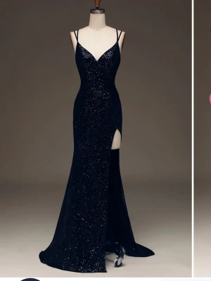 Svart glittrig paljett balklänning med slits - Svart långklänning med glittrigt paljett tyg, smala axelband och djup v-ringning. Klänningen har en hög slits framtill och figurnära passform som framhäver siluetten. Perfekt för bal eller festliga tillfällen. Endast använd en gång.