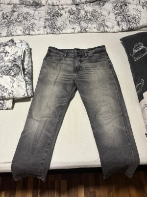 Gråa Hugo Boss jeans - Säljer ett par grå jeans från Hugo Boss med rak passform och snyggt tvättad effekt. Jeansen har klassisk femficksdesign och normal midja. Perfekta för dig som gillar en avslappnad och stilren vibe.