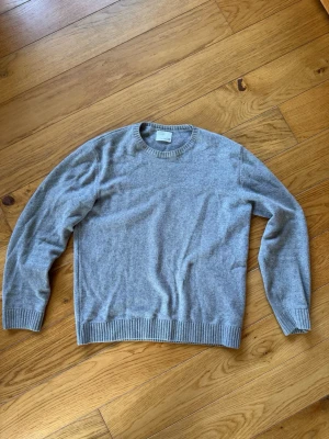 Grå stickad tröja från Colorful standard - Klassisk grå stickad tröja från Colorful standard i mjuk ullblandning. Tröjan har rund halsringning, ribbade muddar vid ärmslut och nederkant samt en enkel, stilren design som passar till det mesta.