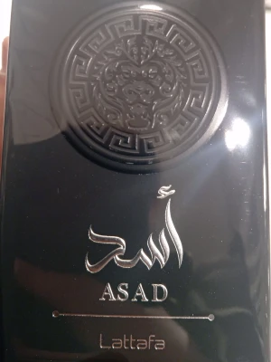 Lattafa Asad Eau de Parfum 100ml - Lattafa Asad Eau de Parfum kommer i en lyxig svart flaska med gulddetaljer och ett lejonmotiv på framsidan. Flaskan har en elegant och modern design med arabiska inskriptioner och guldaccenter som ger en exklusiv känsla. Perfekt för dig som gillar unika och kraftfulla dofter.